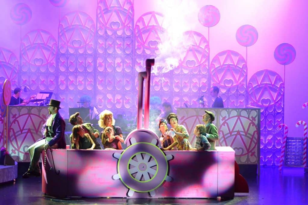 Willie Wonka production in Dubai, UAE. Kids and parents are sat in Wonka's magical boat looking worried with Wonka sat on the front of the boat on stage.